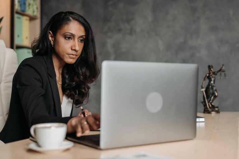 Profissional usando um laptop em um escritório, com uma balança da Justiça sobre a mesa.